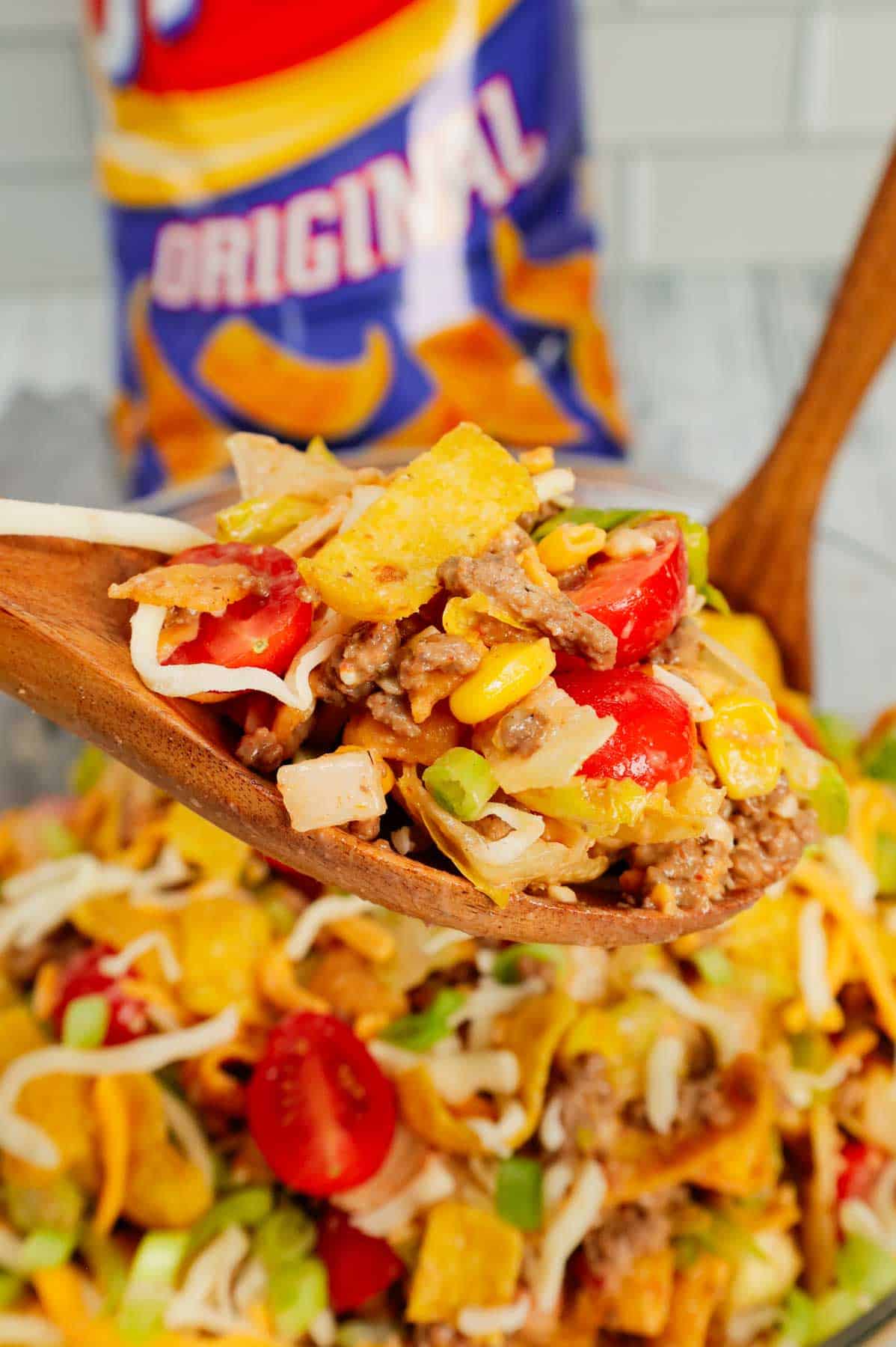 Frito Taco Salad is a delicious meal or side dish recipe loaded with ground beef, taco seasoning, lettuce, red onions, green peppers, grape tomatoes, corn, shredded cheese, salsa, ranch dressing and Fritos corn chips.