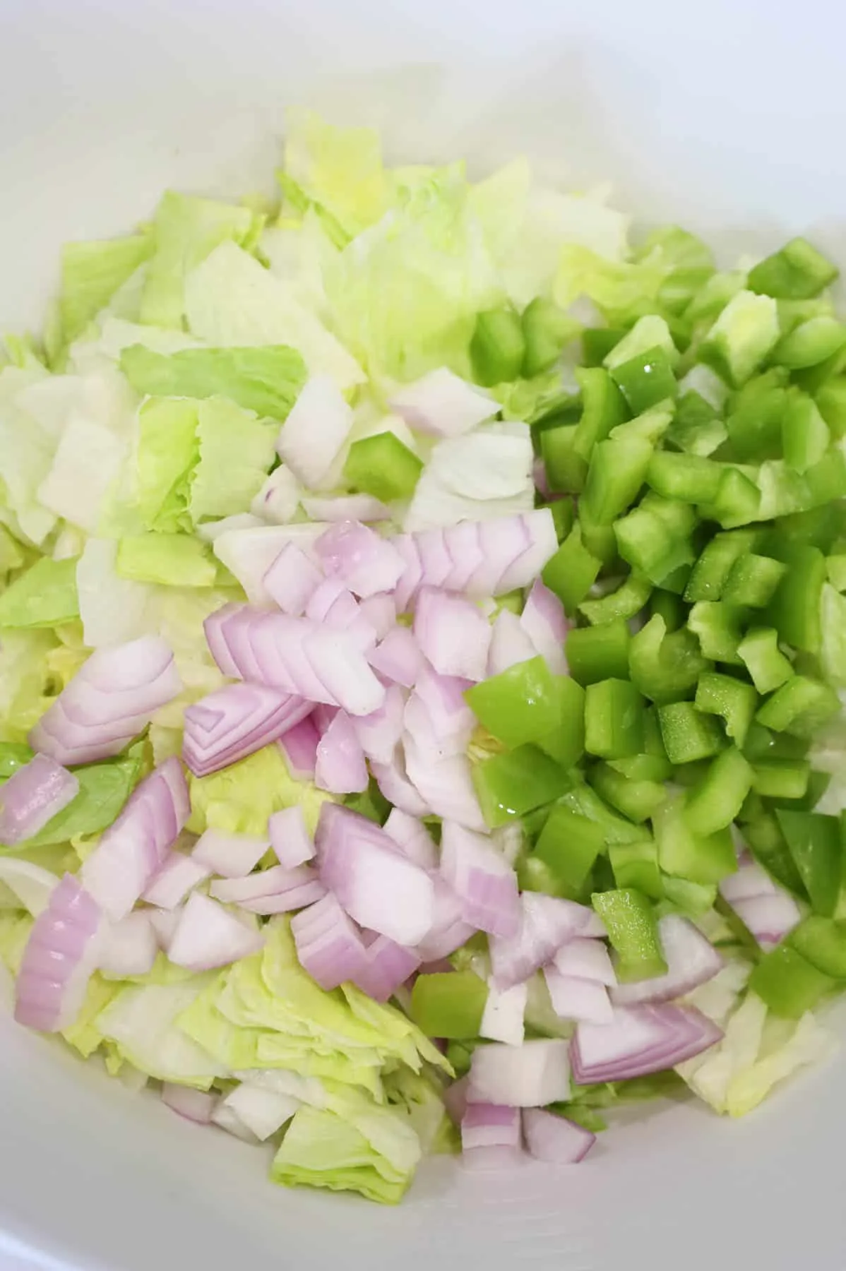diced green peppers and onions on top of chopped lettuce in a bowl