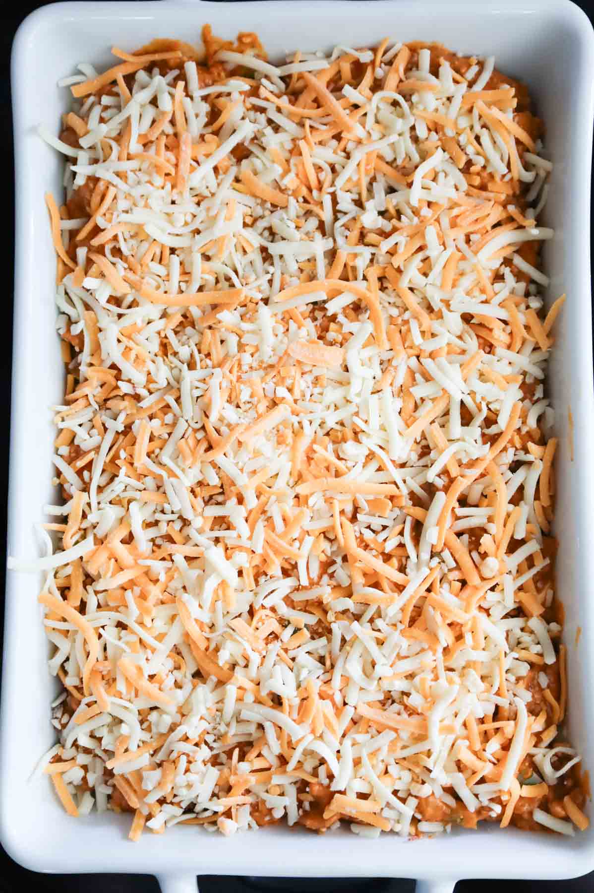 shredded cheese on top of ground beef casserole in a baking dish