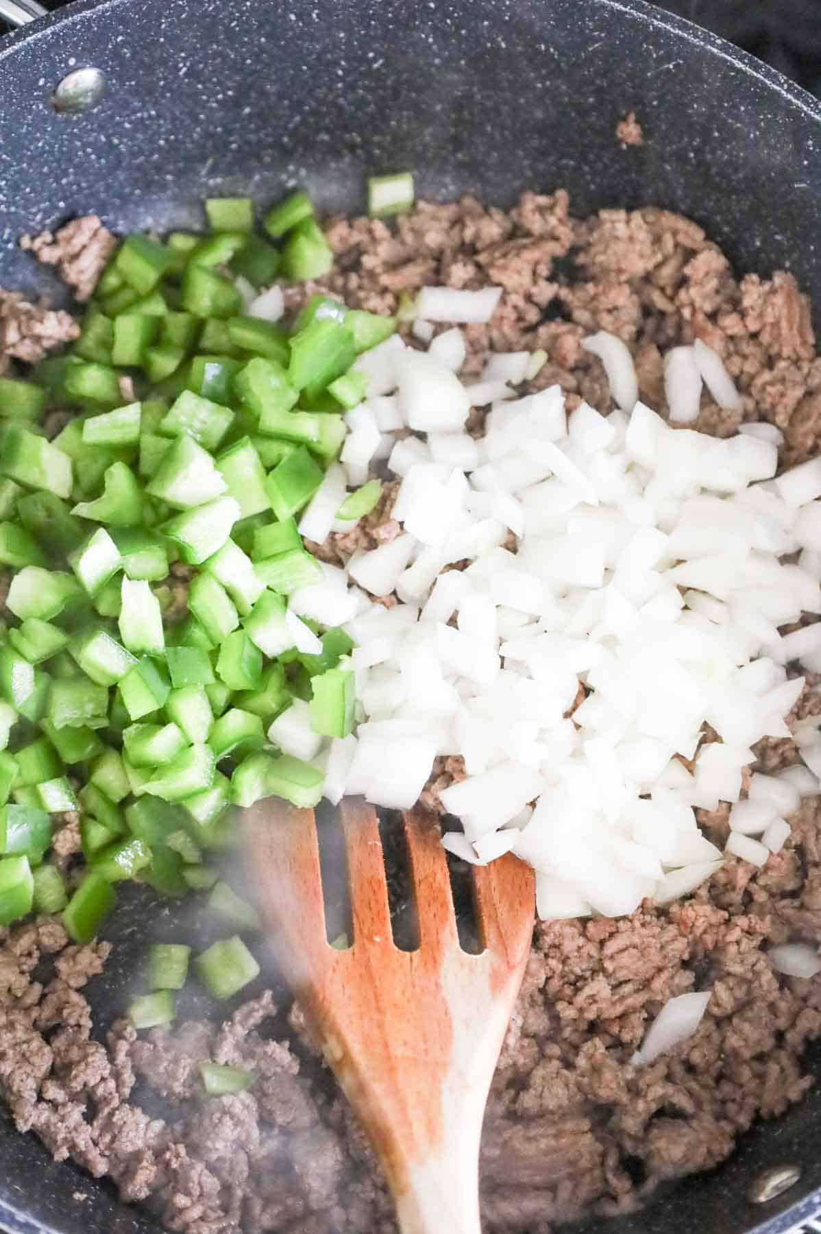 diced green peppers and onions on top of cooked ground beef in a skillet