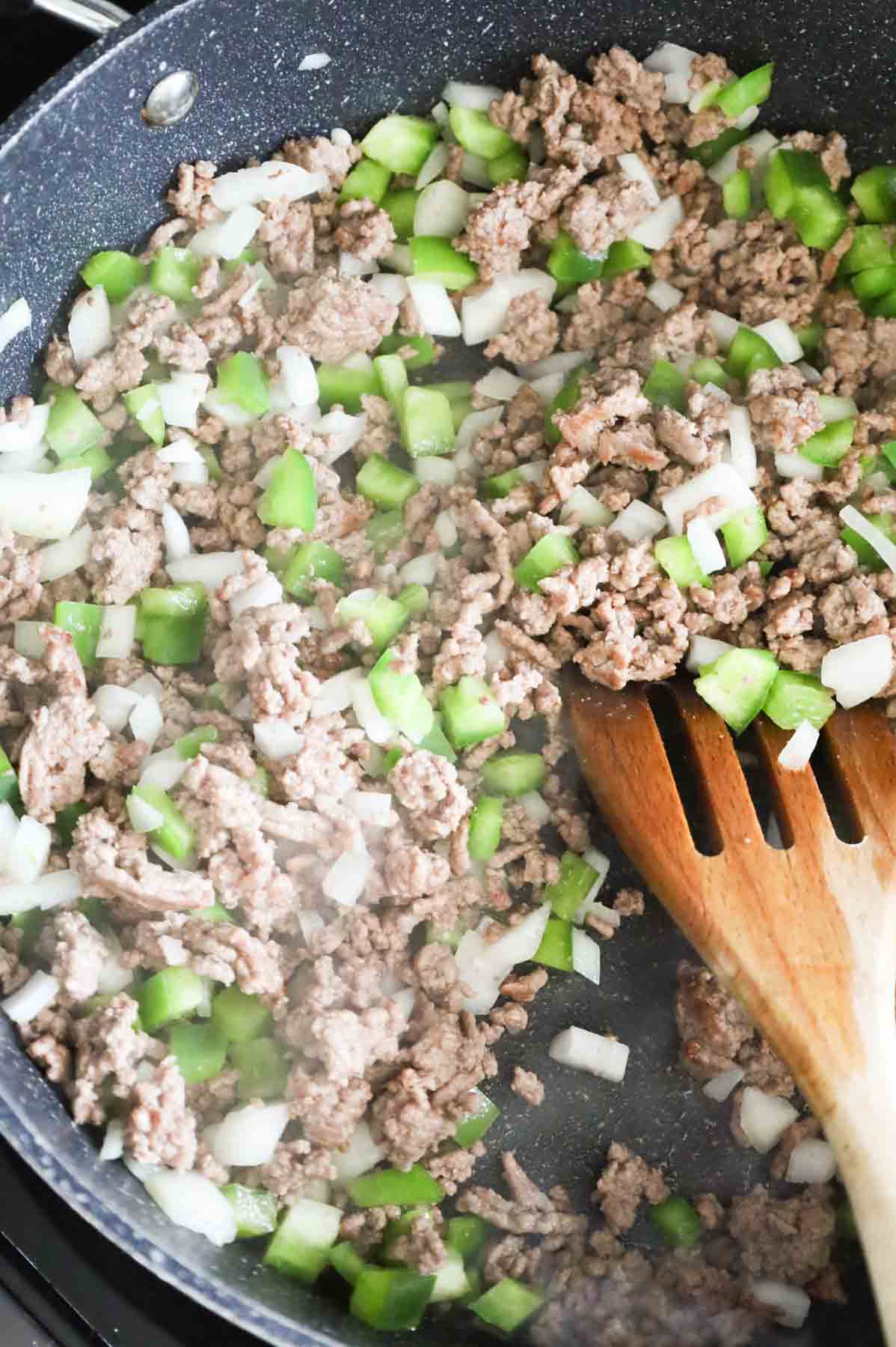 ground beef, diced green peppers and onions cooking in a skillet