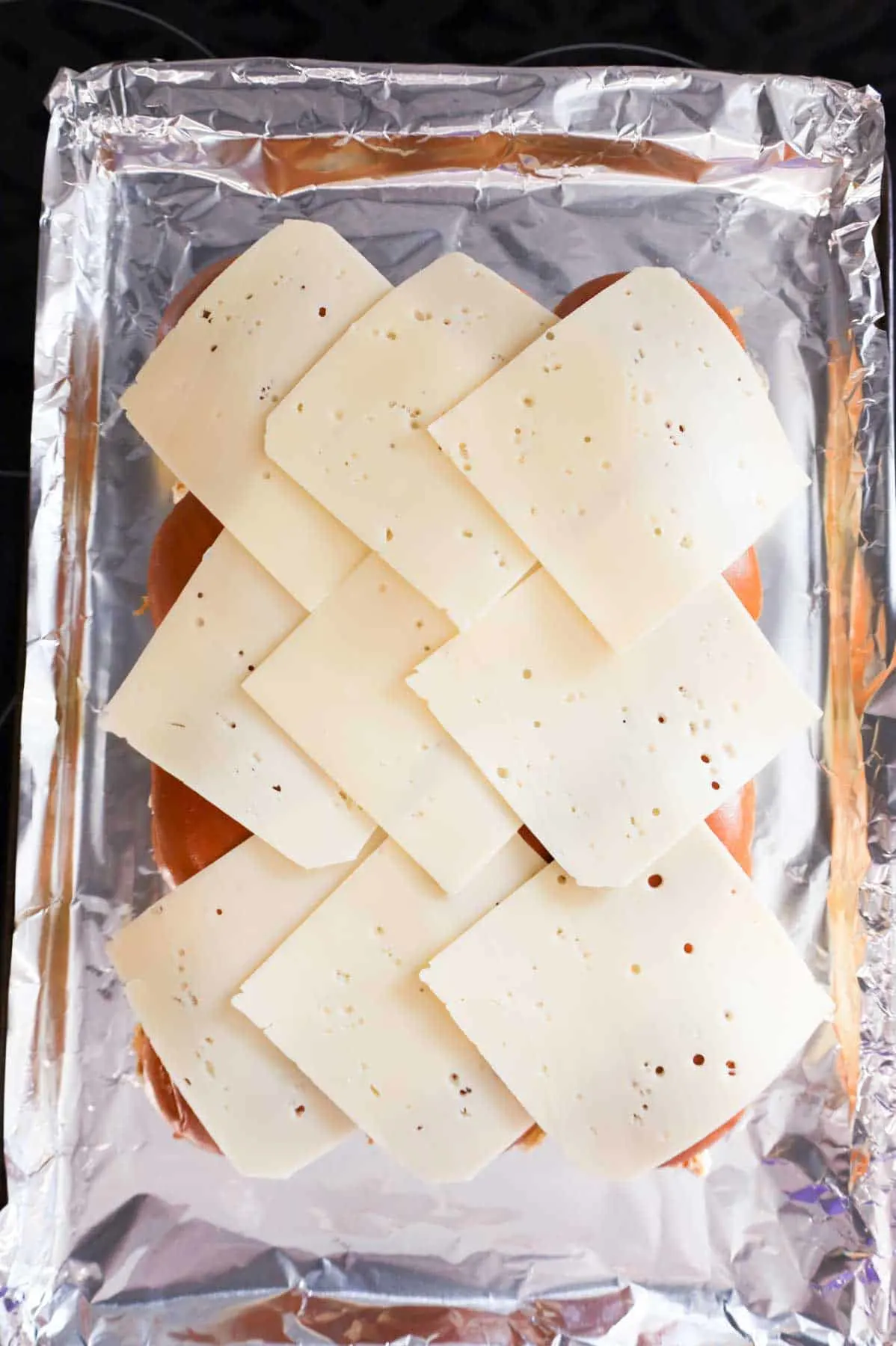 Swiss cheese slices on dinner rolls on a baking sheet