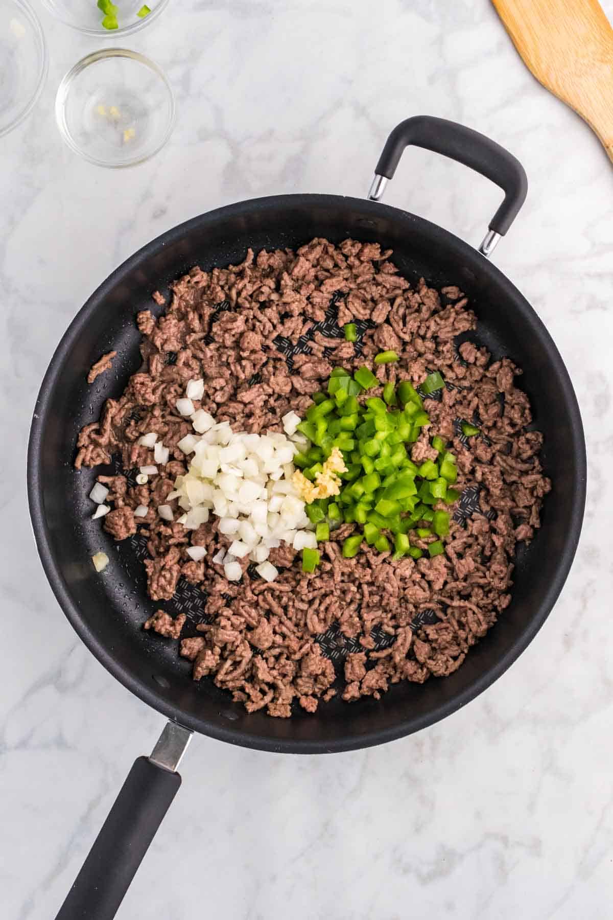 diced onion, minced garlic and diced green bell peppers on top of cooked ground beef in a skillet