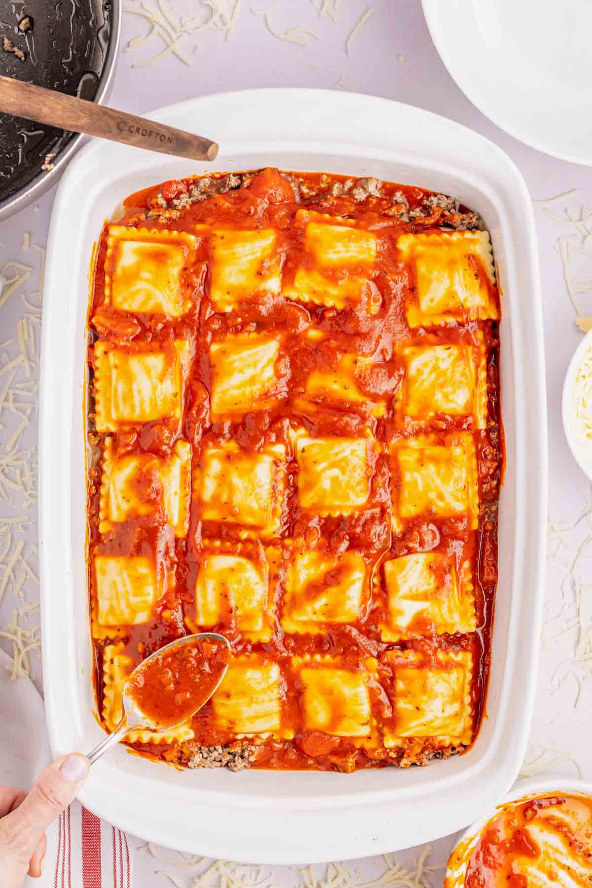 spooning marinara over ravioli in a baking dish