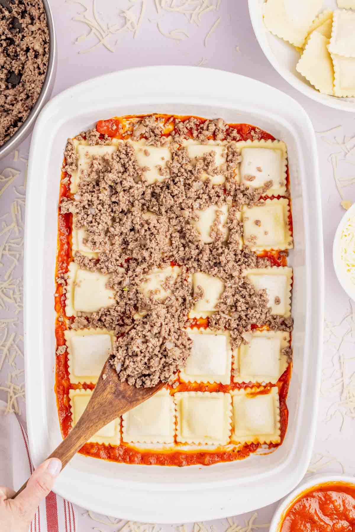 spooning cooked ground beef over ravioli in a baking dish