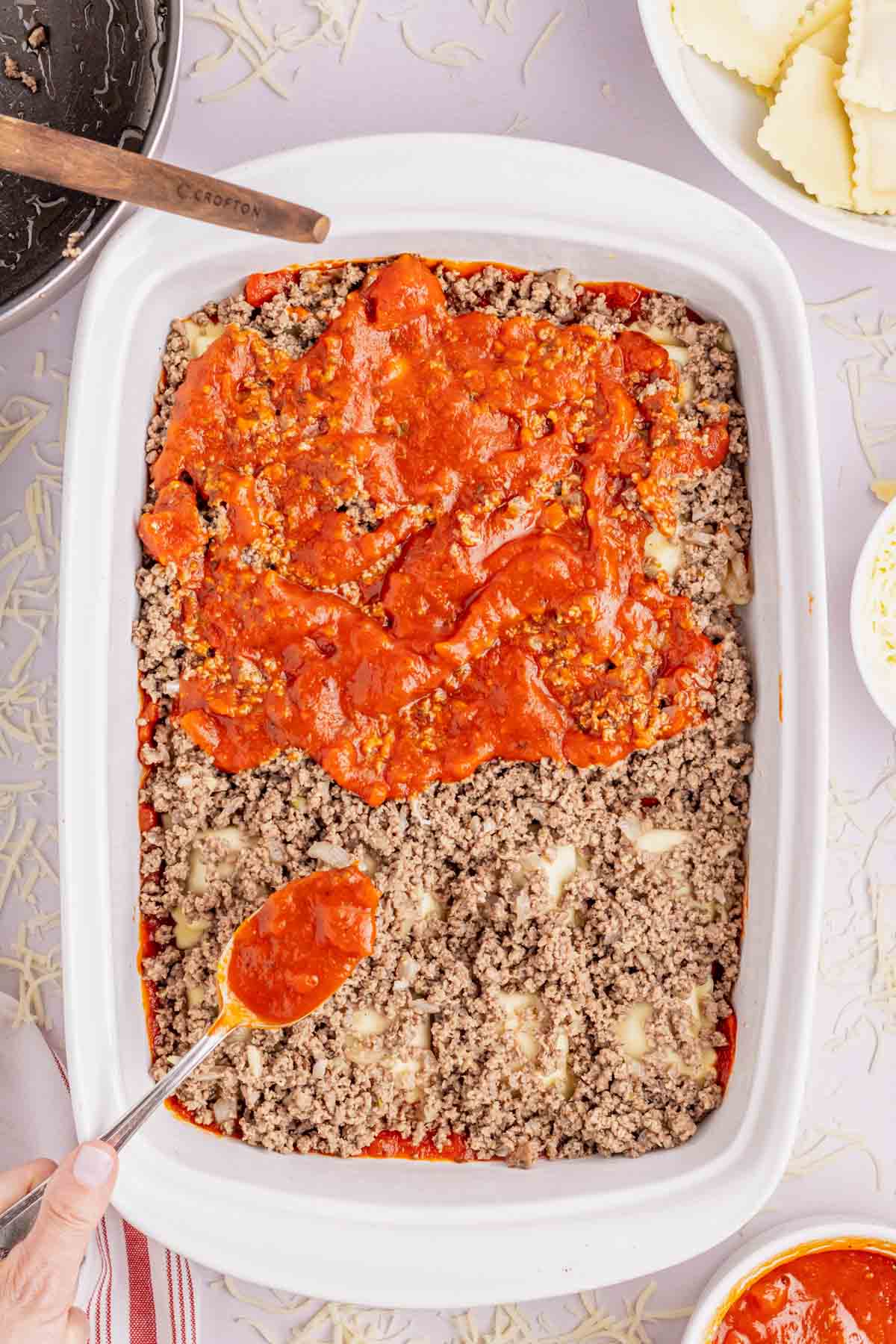 spooning marinara over ground beef in a baking dish