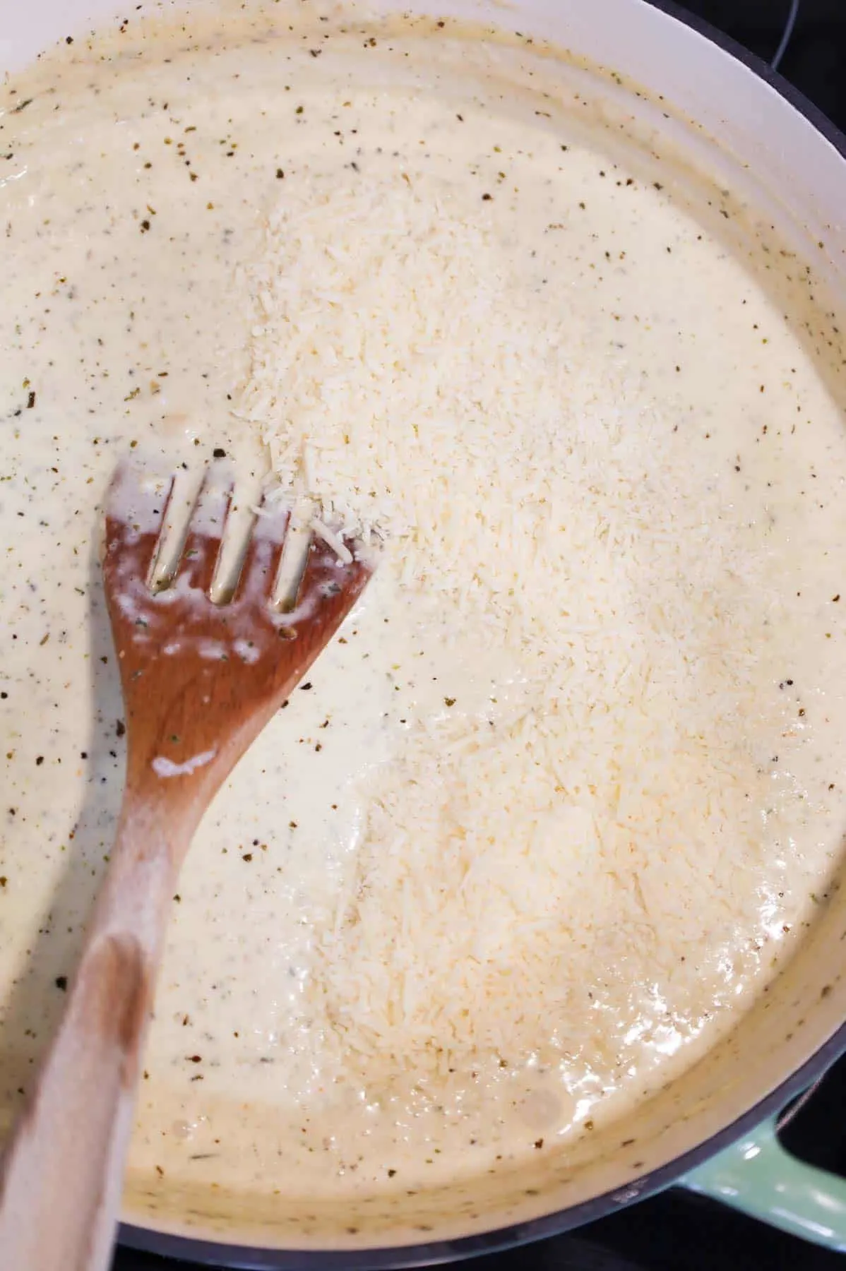 grated parmesan added to alfredo sauce in a skillet