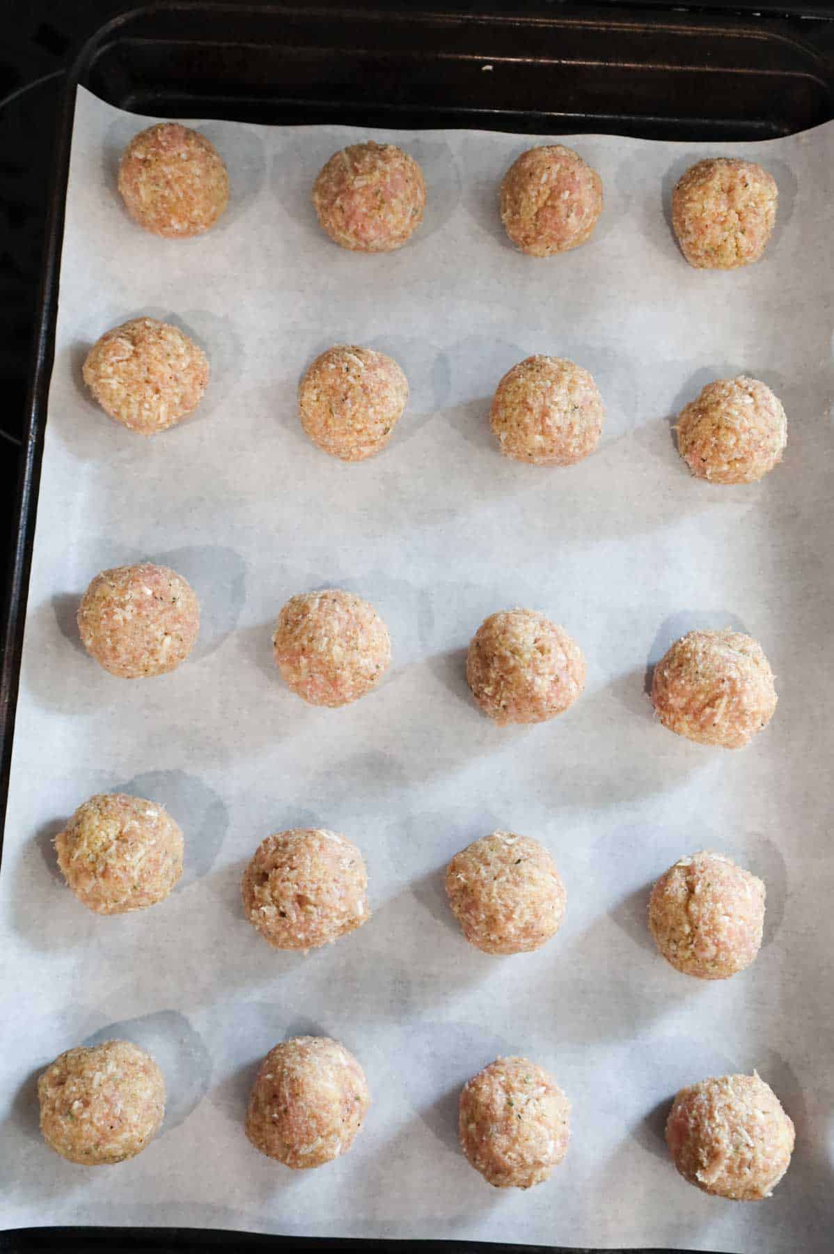 raw chicken meatballs on a parchment lined baking sheet