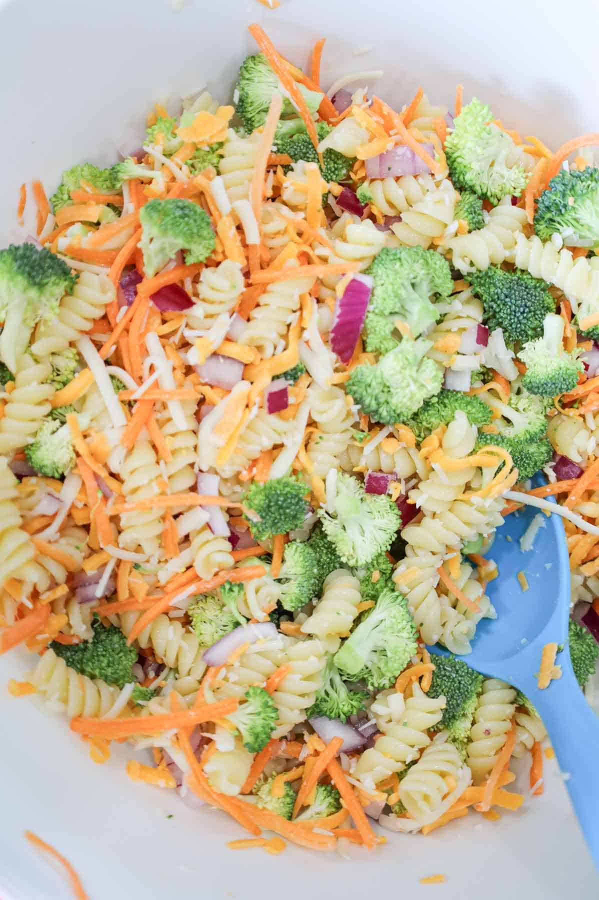 broccoli pasta salad being stirred in a mixing bowl