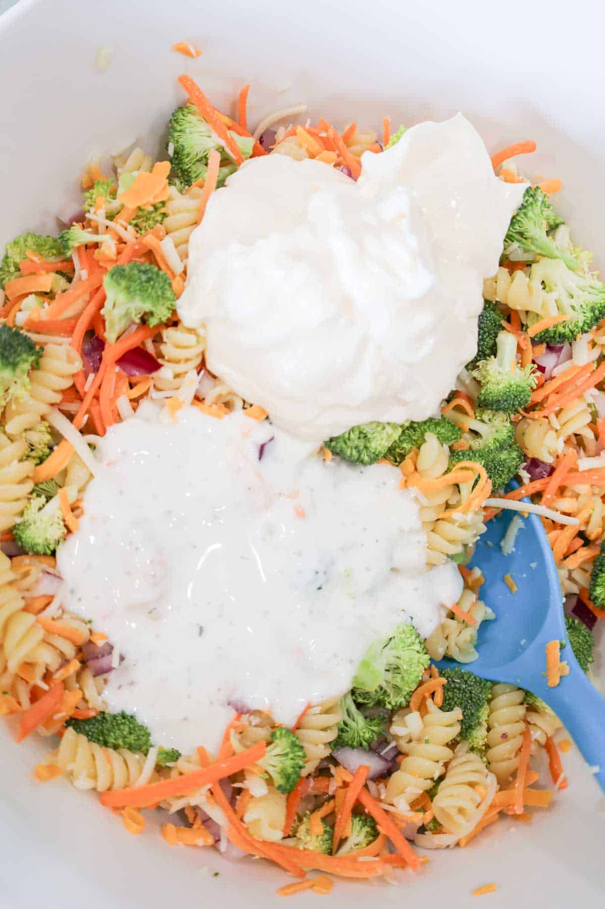 mayo and ranch dressing on top of broccoli pasta salad in a bowl