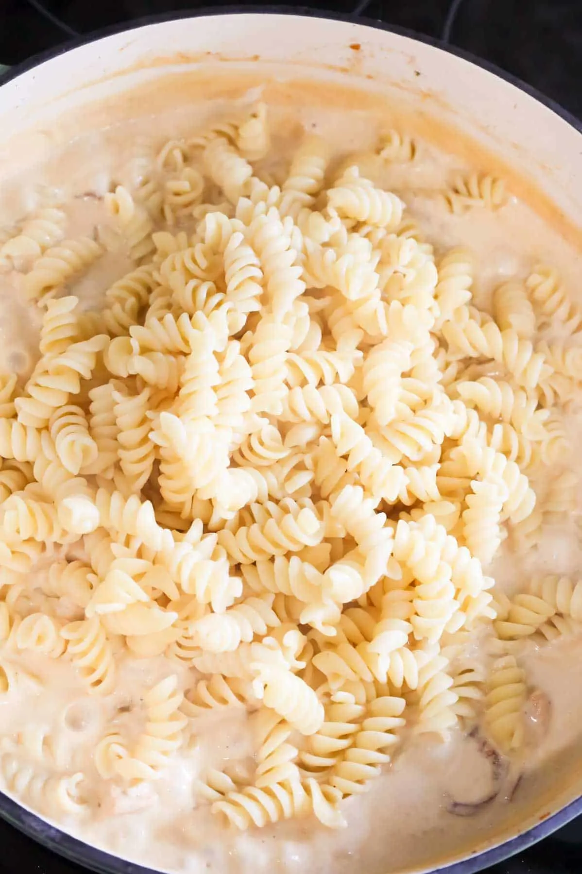 cooked rotini noodles added to a skillet with creamy alfredo sauce