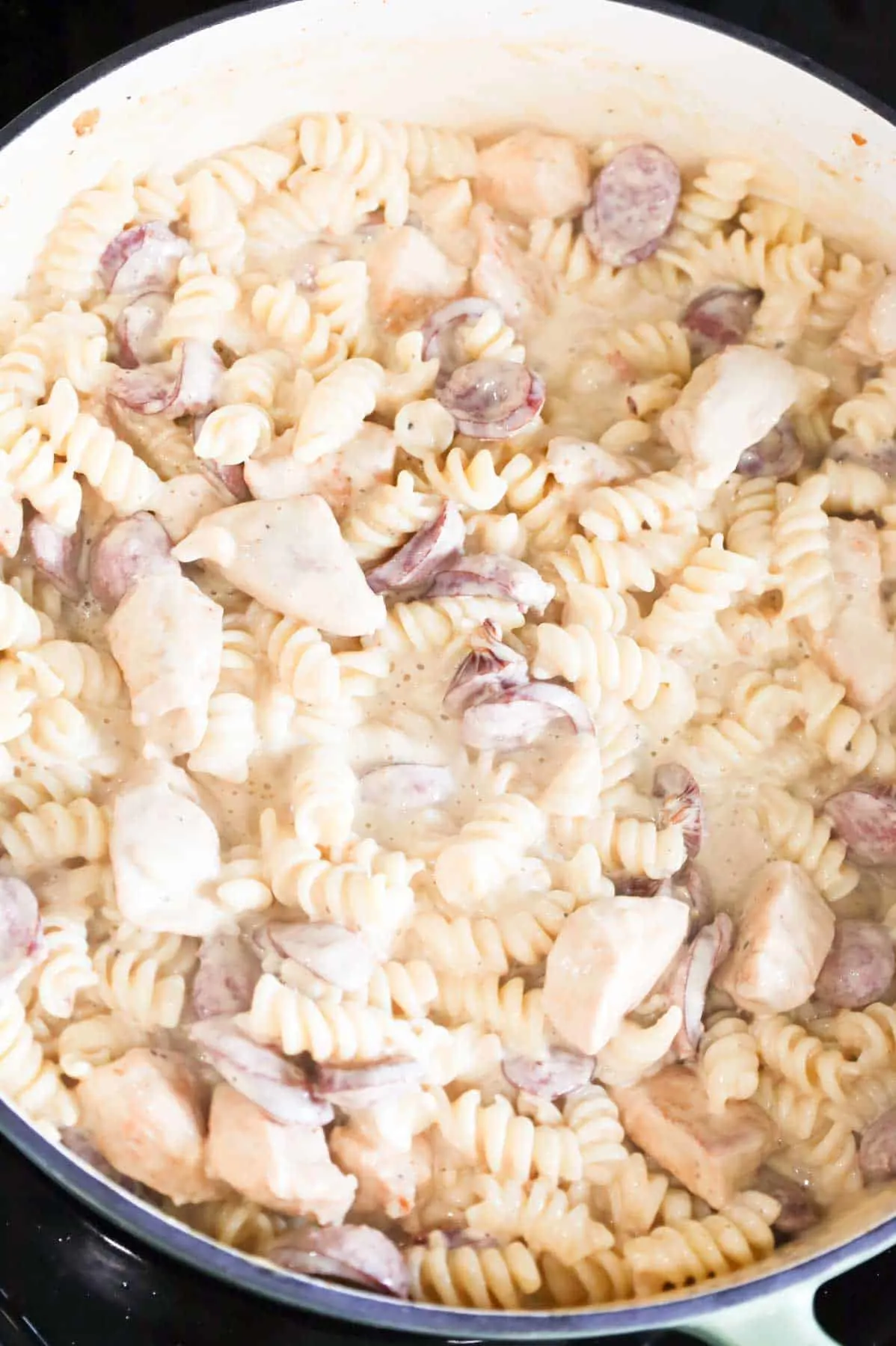 rotini noodles stirred into creamy alfredo sauce in a skillet
