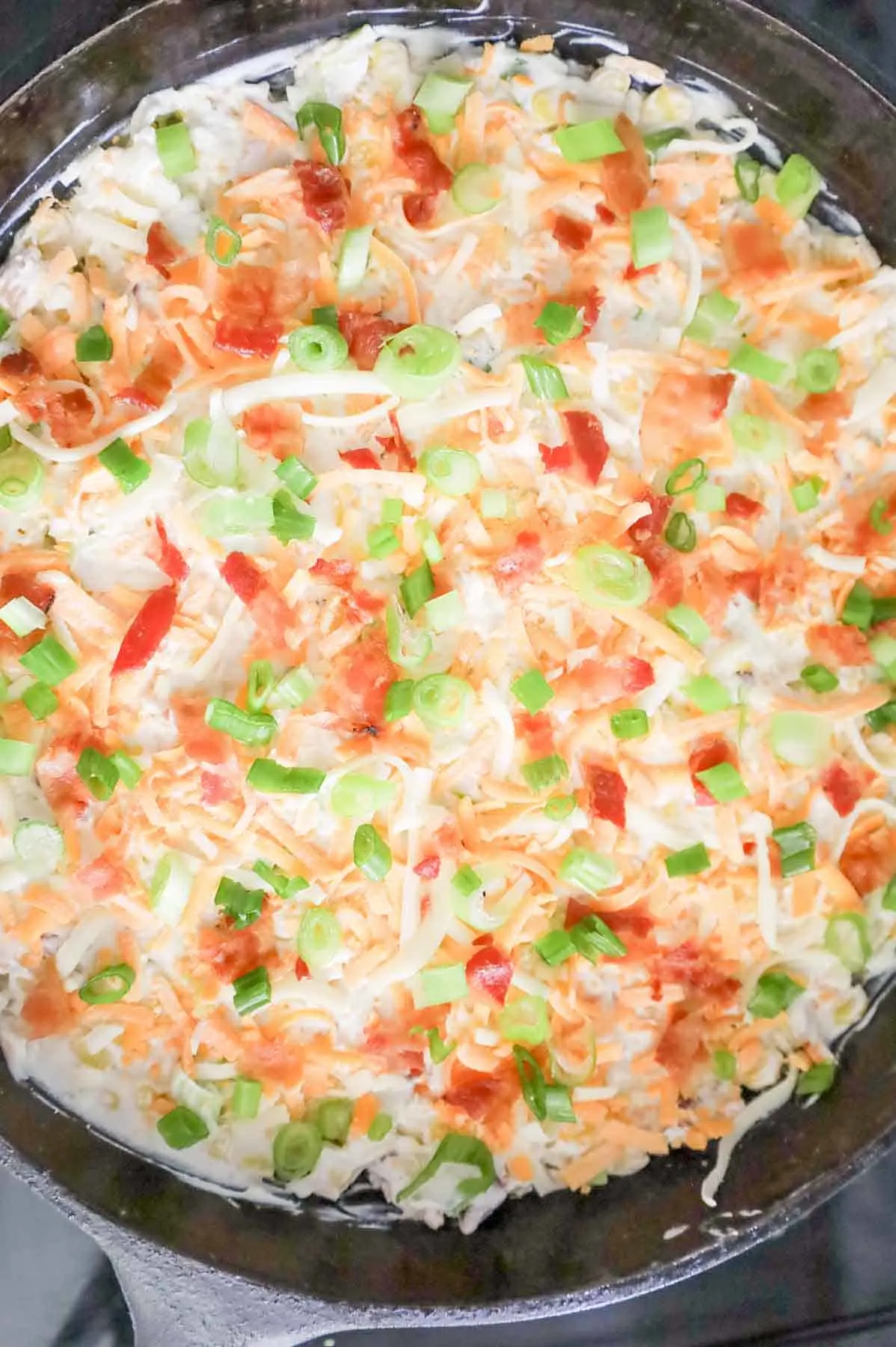 chopped bacon, green onions and shredded cheese on top of corn dip in a skillet