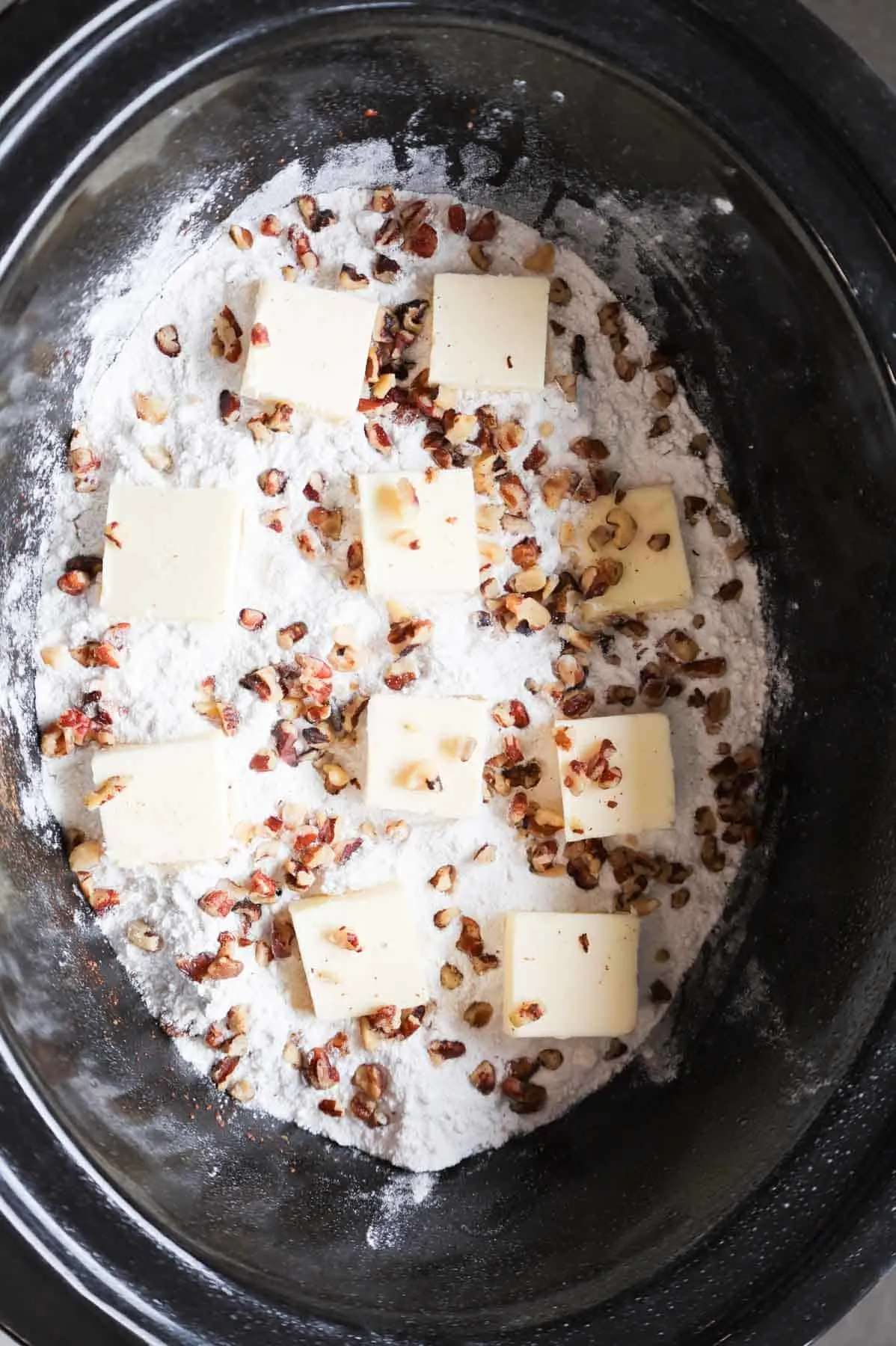 chopped pecans and butter squares on top of cake mix in a crock pot