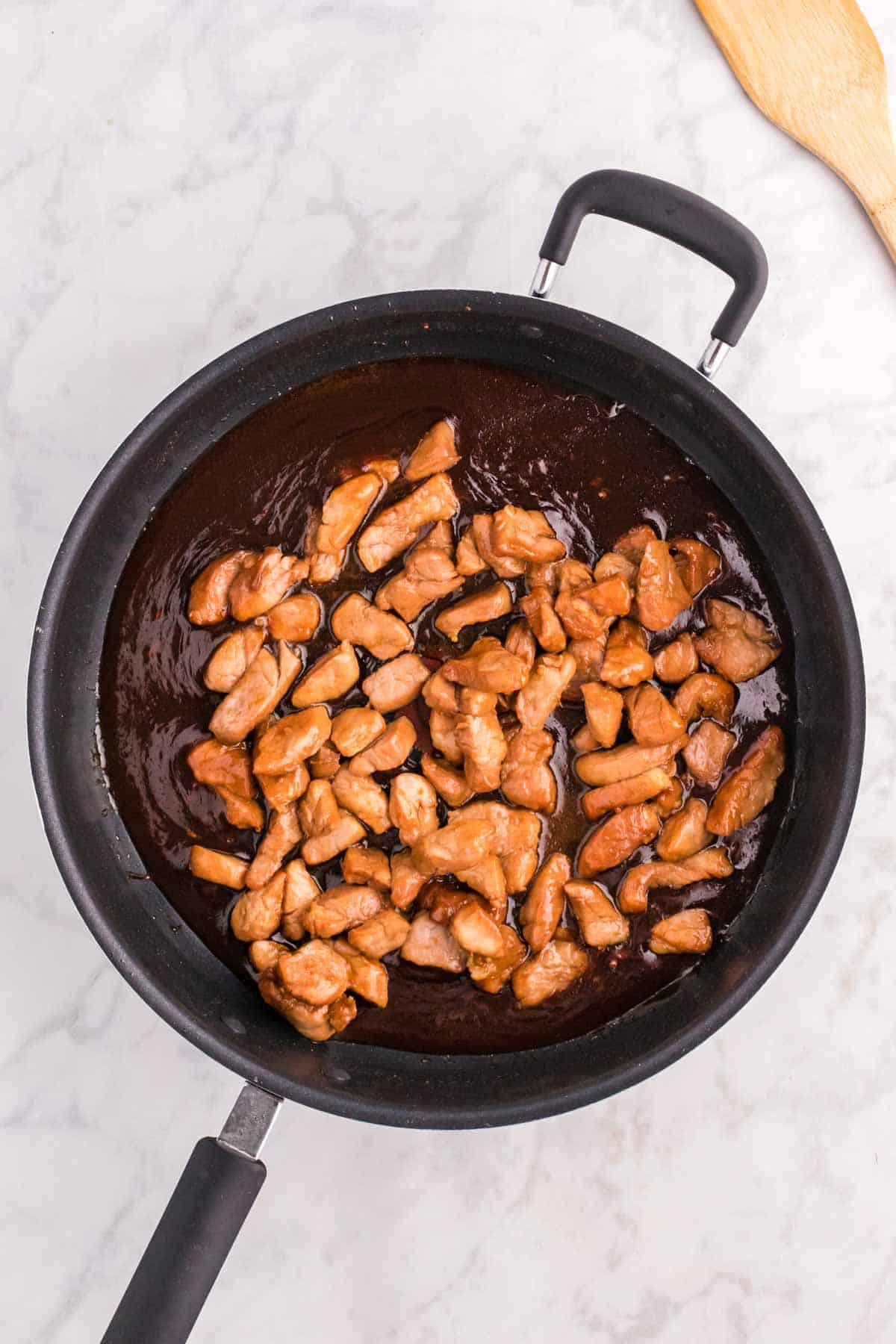 cooked pork pieces added to a skillet with a simmering sauce