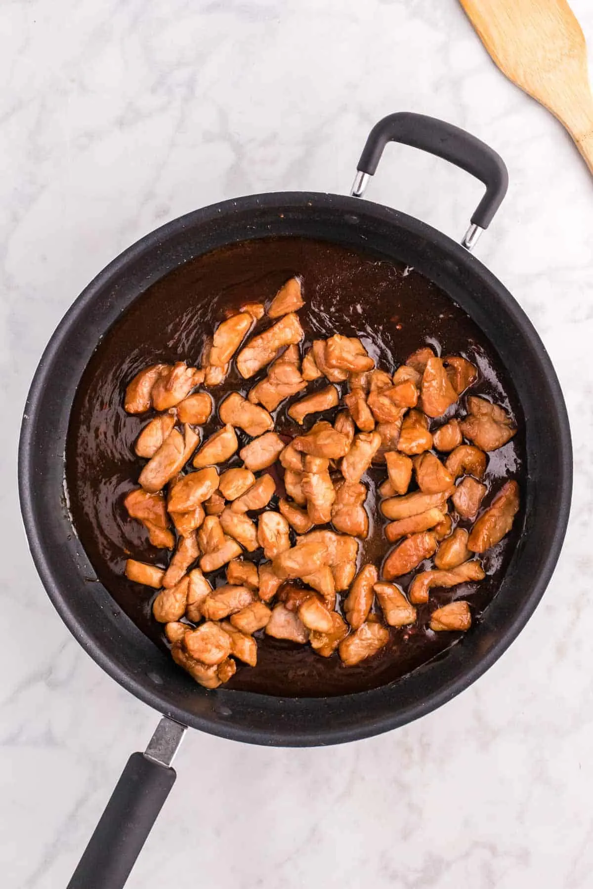 cooked pork pieces added to a skillet with a simmering sauce