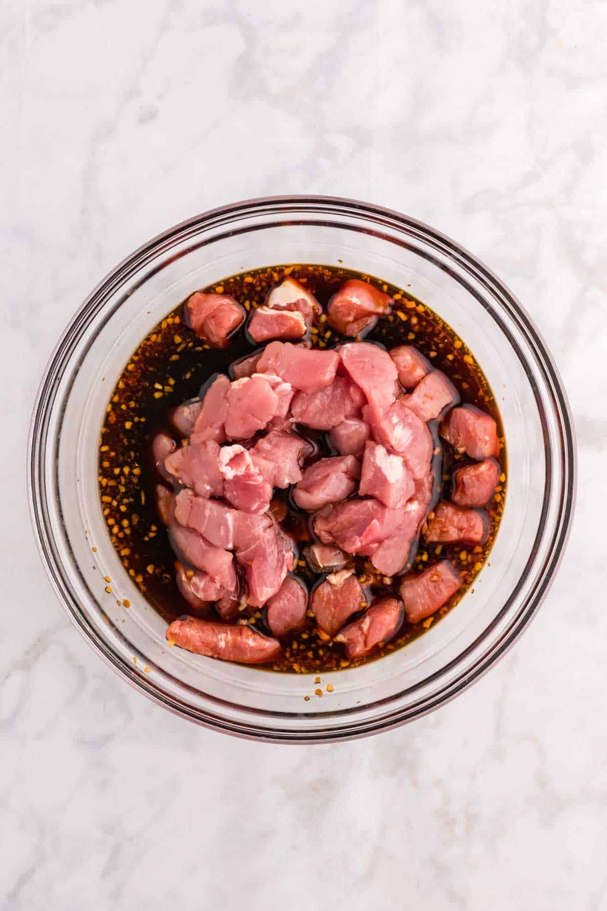 pork pieces added to a bowl with marinade