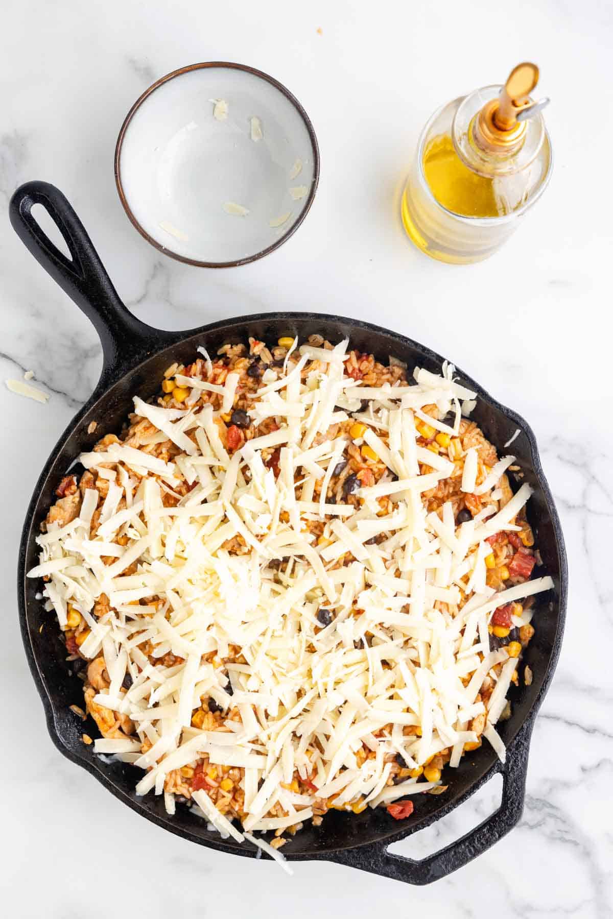 shredded cheese on top of chicken and rice in a skillet