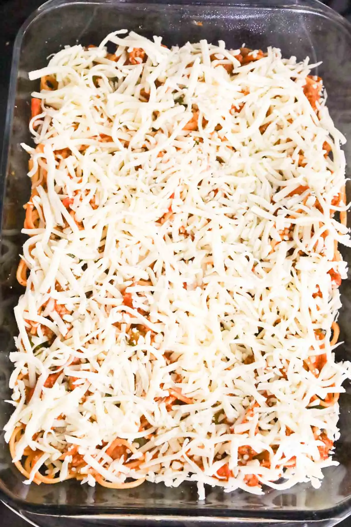 shredded mozzarella on top of spaghetti in a baking dish