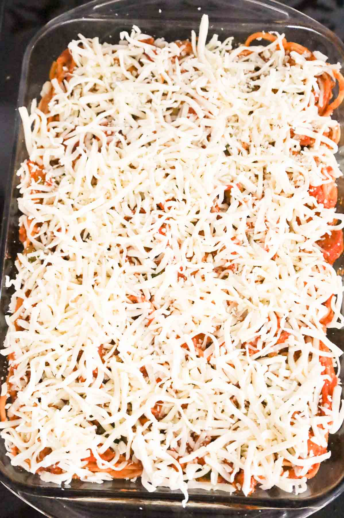 shredded mozzarella cheese on top of pepperoni spaghetti in a baking dish