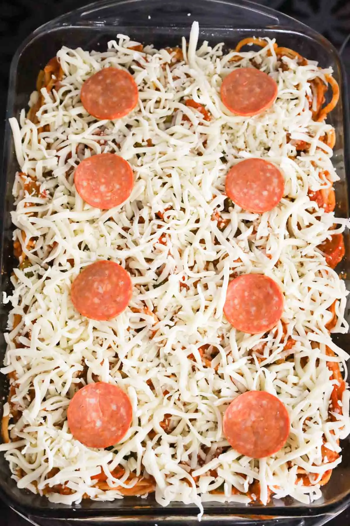 pepperoni slices on top of shredded mozzarella cheese and spaghetti in a baking dish