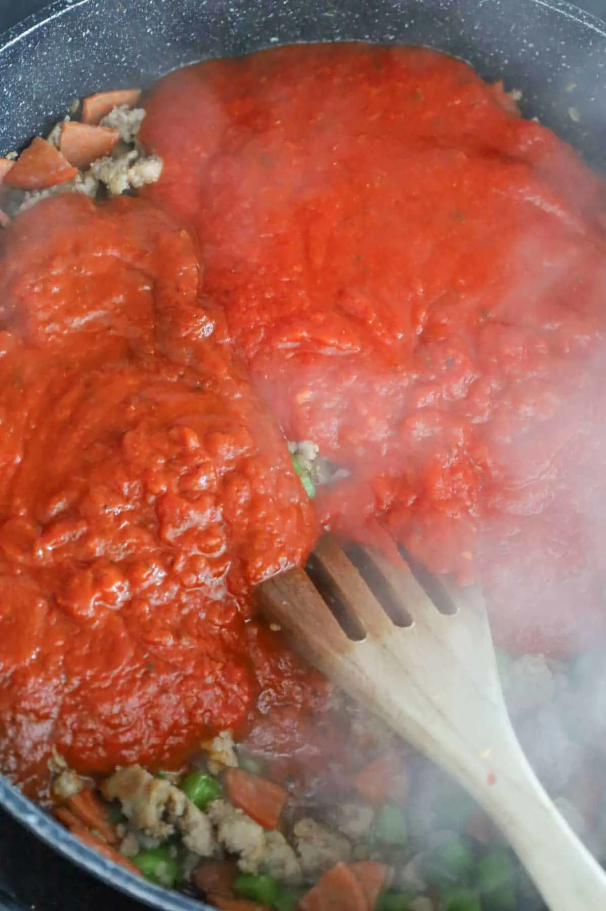 pizza sauce and marinara sauce on top of cooked sausage meat in a skillet