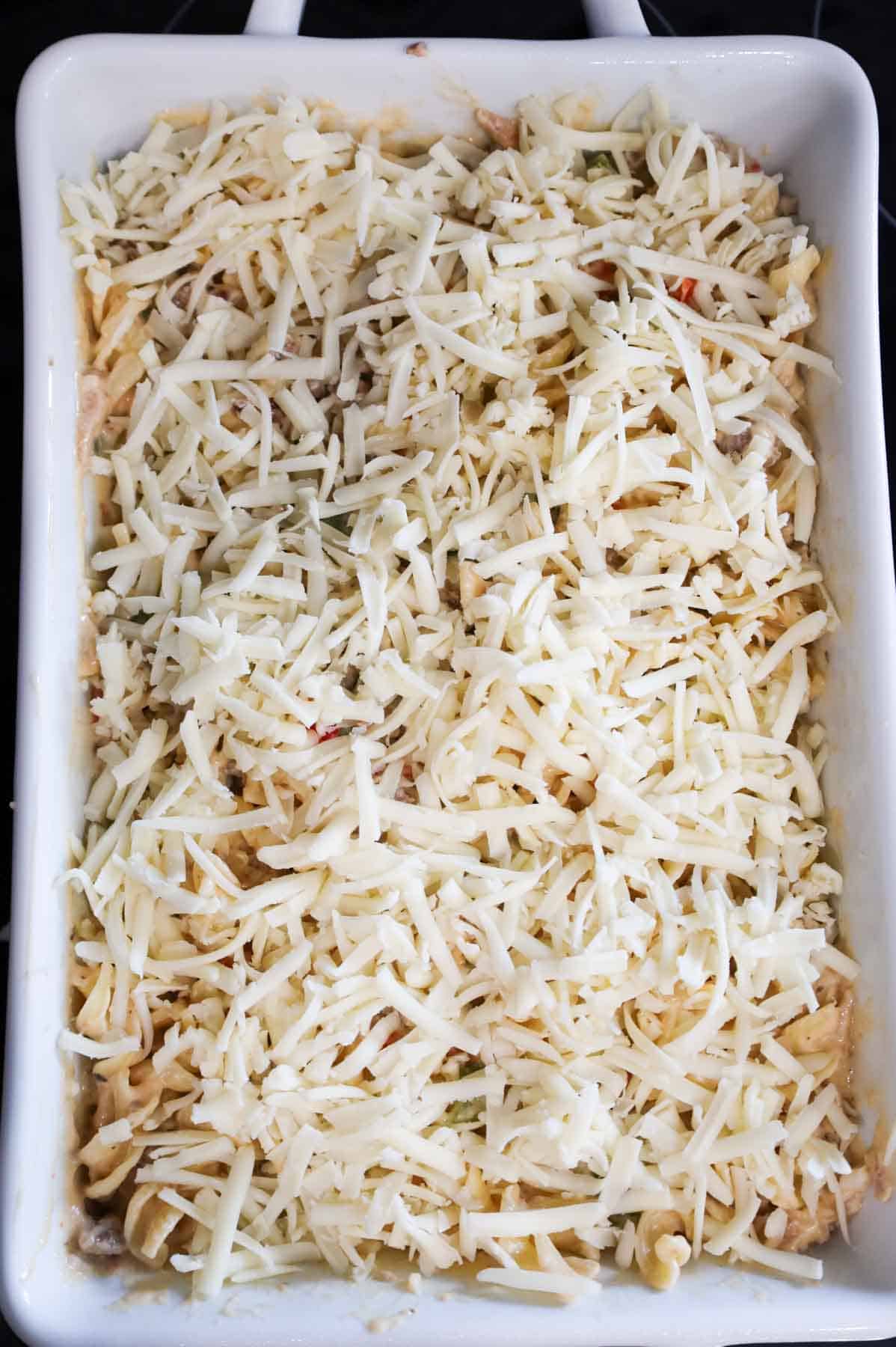 shredded provolone cheese on top of sausage noodle casserole in a baking dish