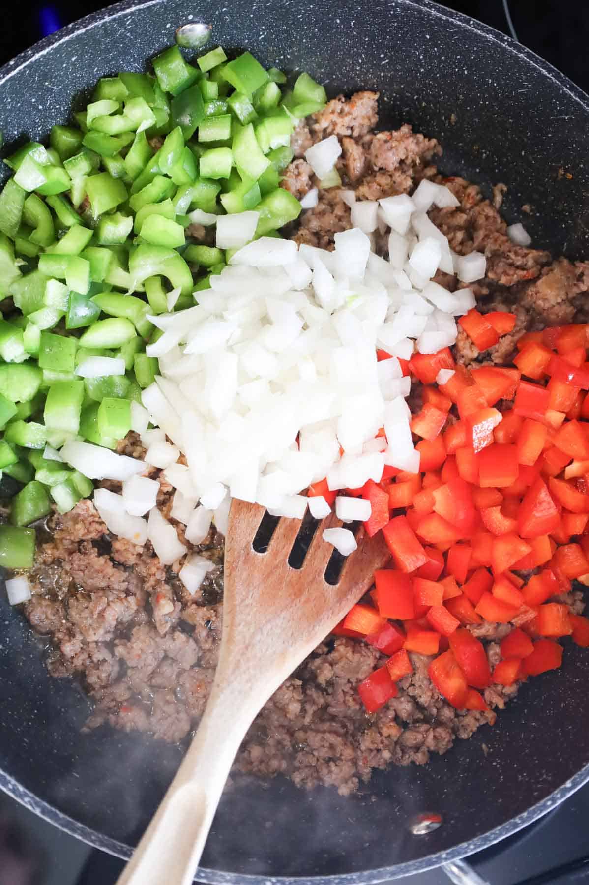 diced green peppers, red peppers and onions on top of crumbled sausage meat in a skillet
