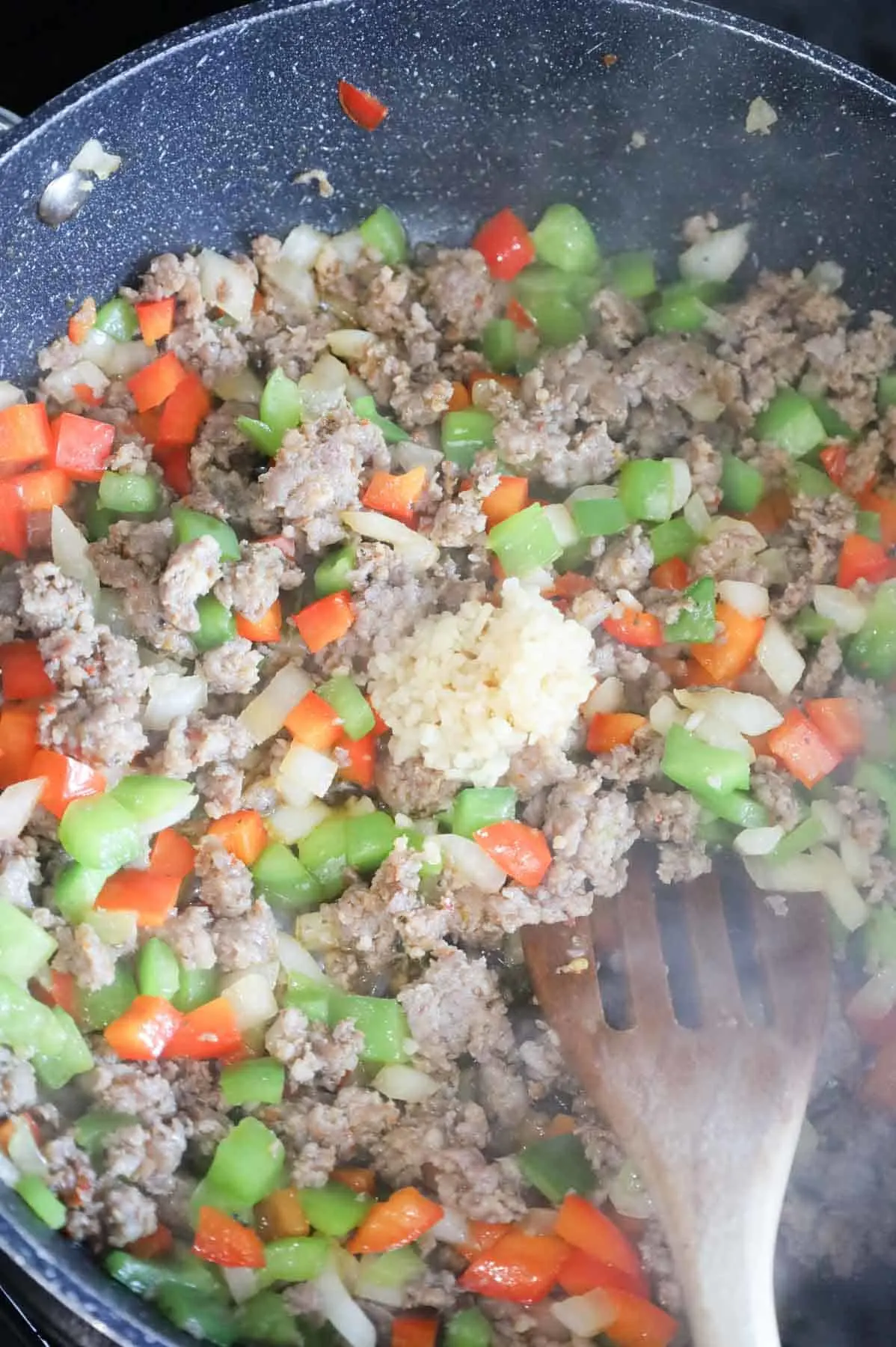 minced garlic on top of sausage and bell pepper mixture in a skillet