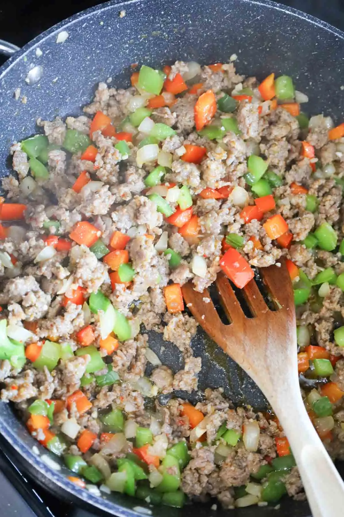 garlic, bell peppers, onions and sausage meat cooking in a skillet