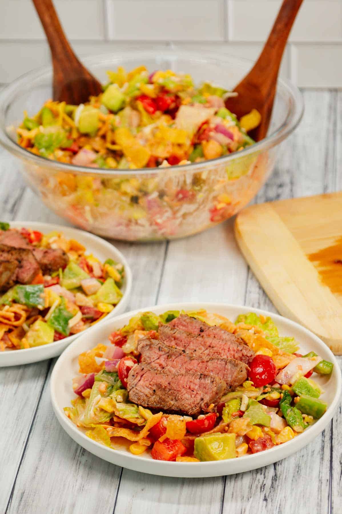 Steak Taco Salad is a delicious dinner recipe loaded with romaine lettuce, red onions, red bell peppers, green bell peppers, grape tomatoes, corn, shredded cheese, chunky salsa, ranch dressing, diced avocado, Fritos corn chips and sliced eye of round steaks.