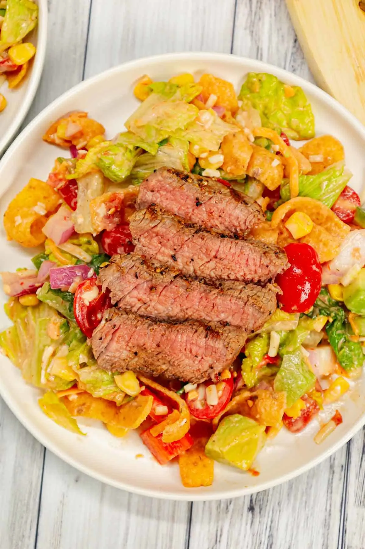 Steak Taco Salad is a delicious dinner recipe loaded with romaine lettuce, red onions, red bell peppers, green bell peppers, grape tomatoes, corn, shredded cheese, chunky salsa, ranch dressing, diced avocado, Fritos corn chips and sliced eye of round steaks.