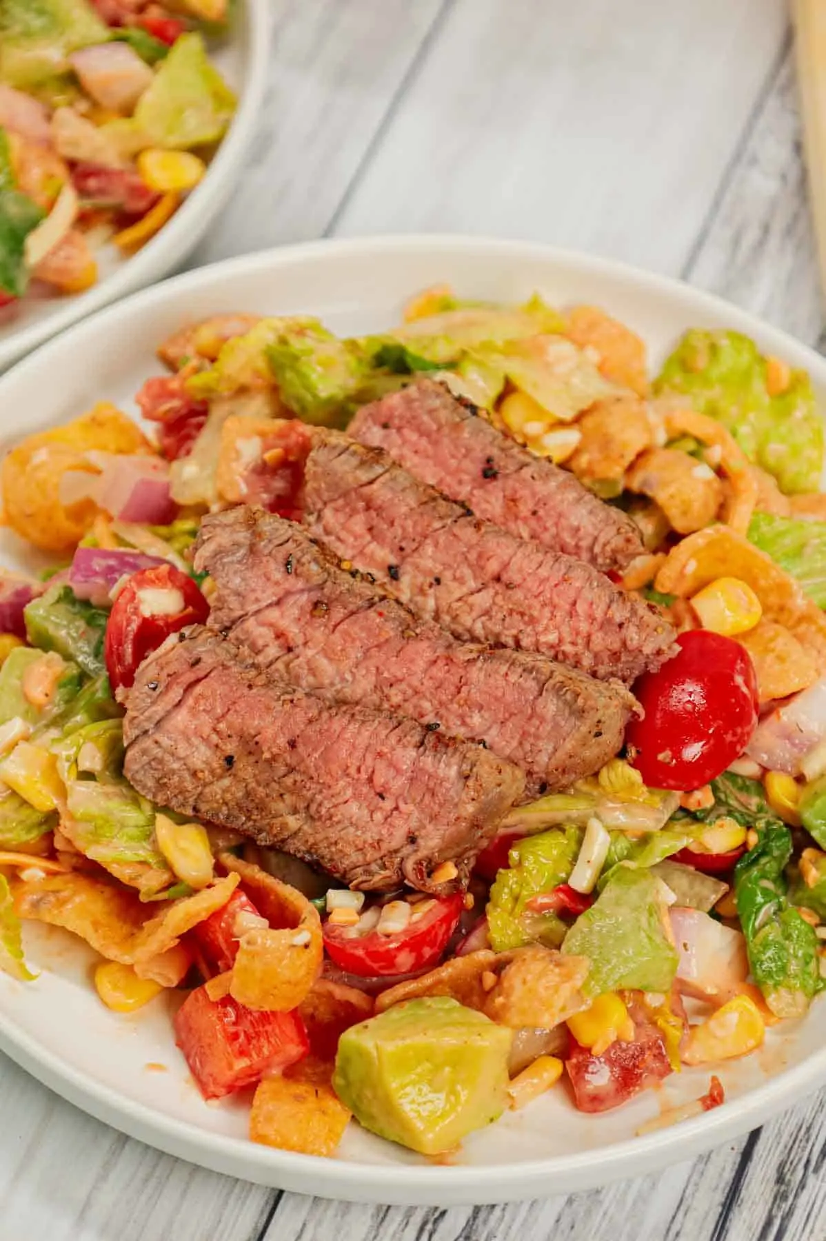 Steak Taco Salad is a delicious dinner recipe loaded with romaine lettuce, red onions, red bell peppers, green bell peppers, grape tomatoes, corn, shredded cheese, chunky salsa, ranch dressing, diced avocado, Fritos corn chips and sliced eye of round steaks.