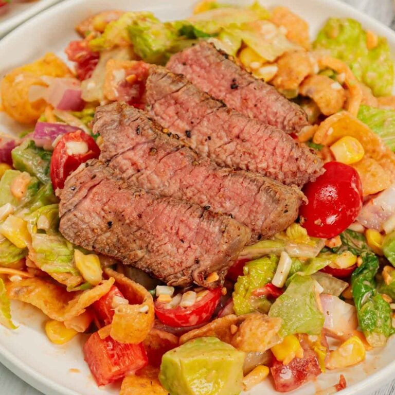 Steak Taco Salad is a delicious dinner recipe loaded with romaine lettuce, red onions, red bell peppers, green bell peppers, grape tomatoes, corn, shredded cheese, chunky salsa, ranch dressing, diced avocado, Fritos corn chips and sliced eye of round steaks.