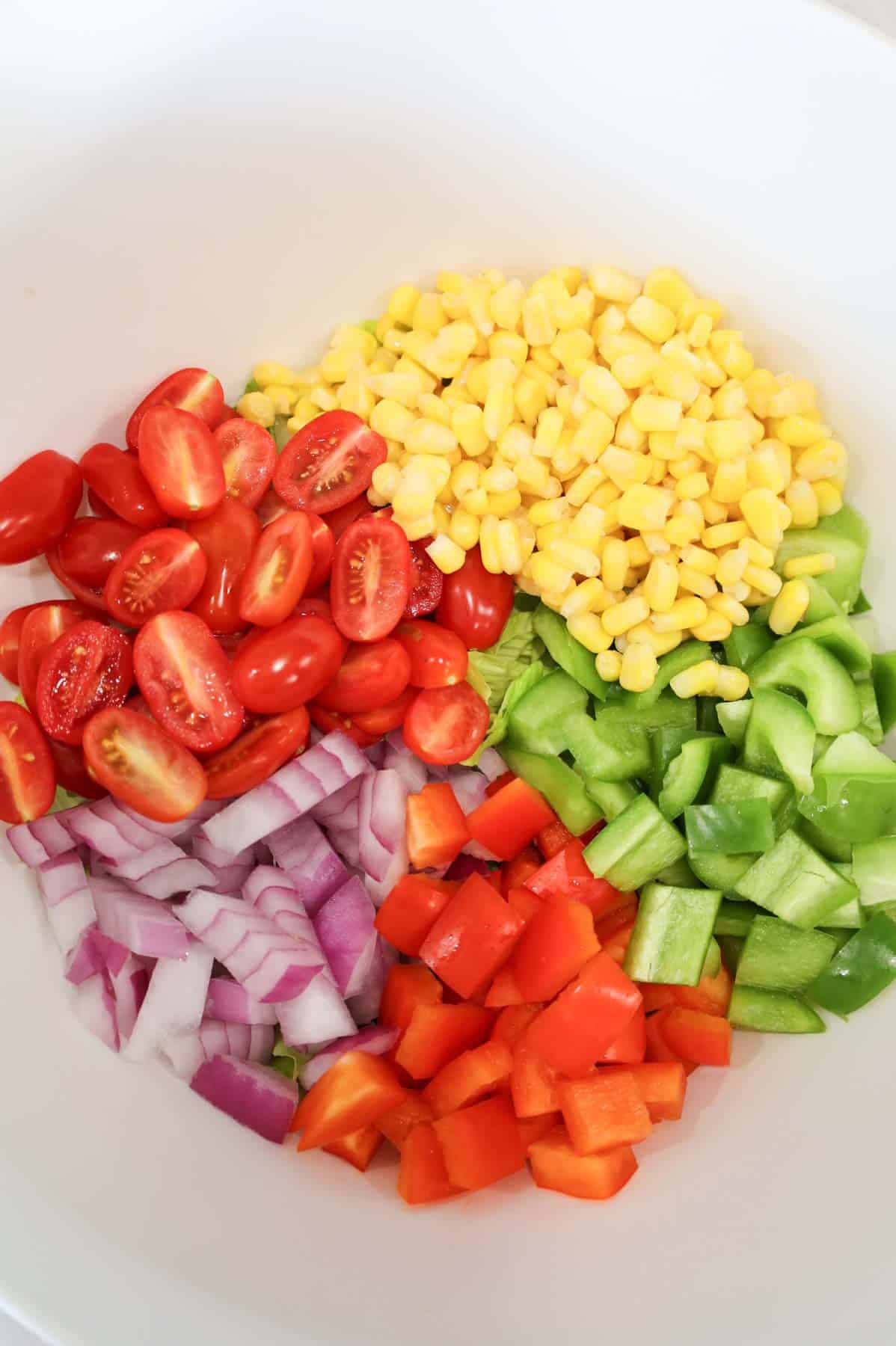 halved grape tomatoes, corn, red onions, red and green bell peppers in a bowl