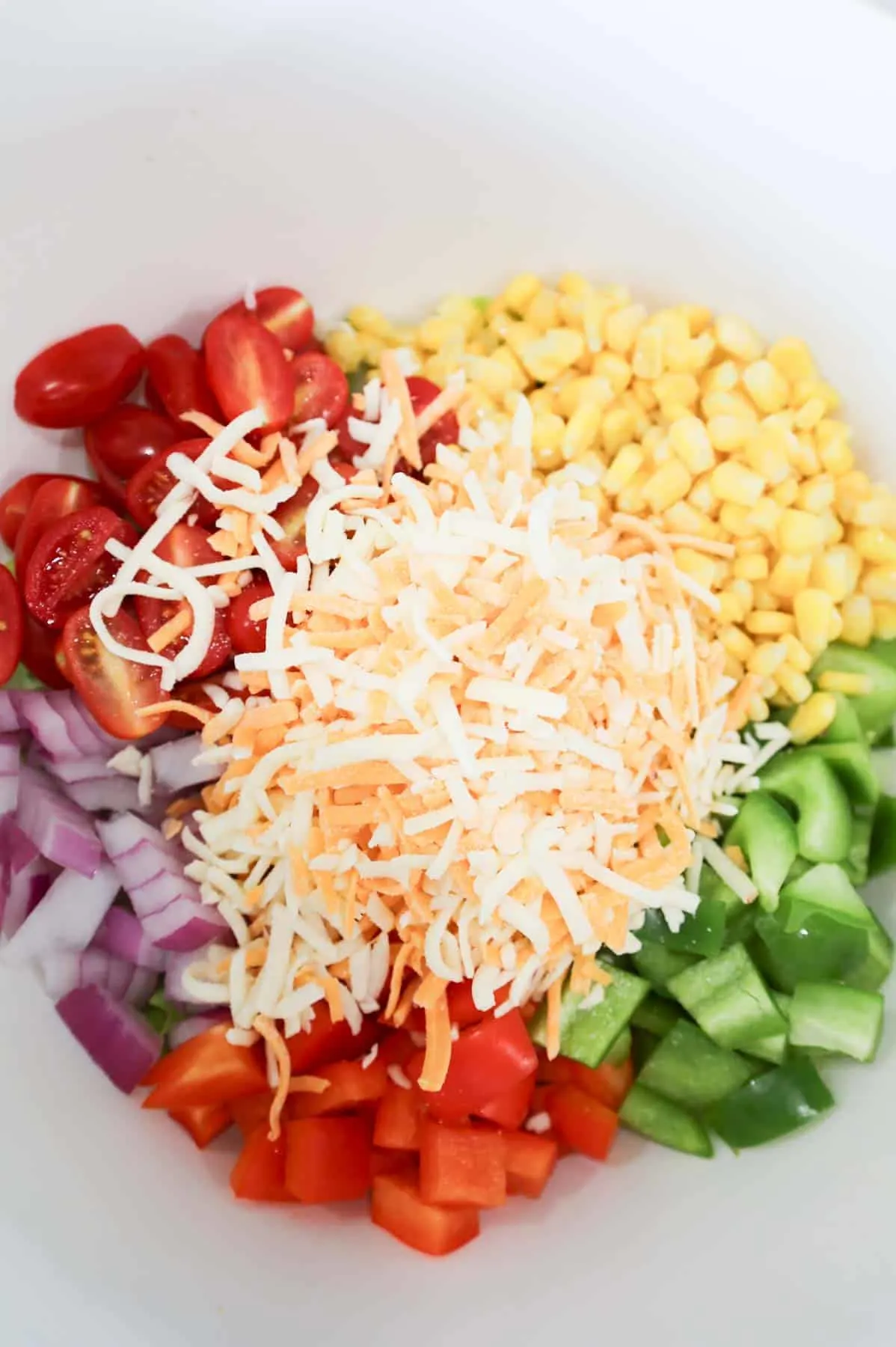 shredded cheese, halved grape tomatoes, red onions, red and green bell peppers and corn in a bowl