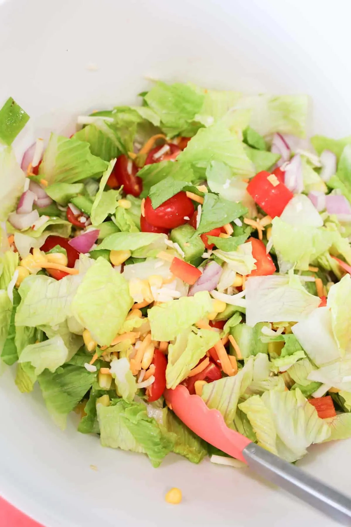 taco salad ingredients being tossed together in a bowl