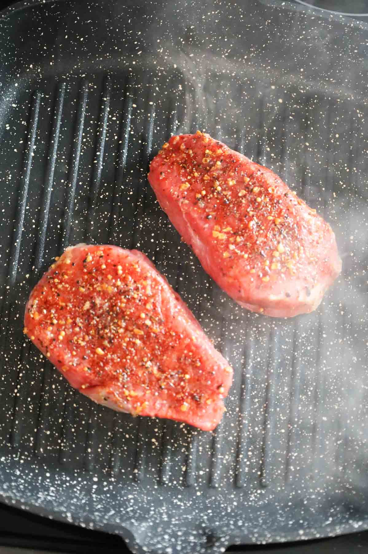 seasoned steaks cooking in a skillet