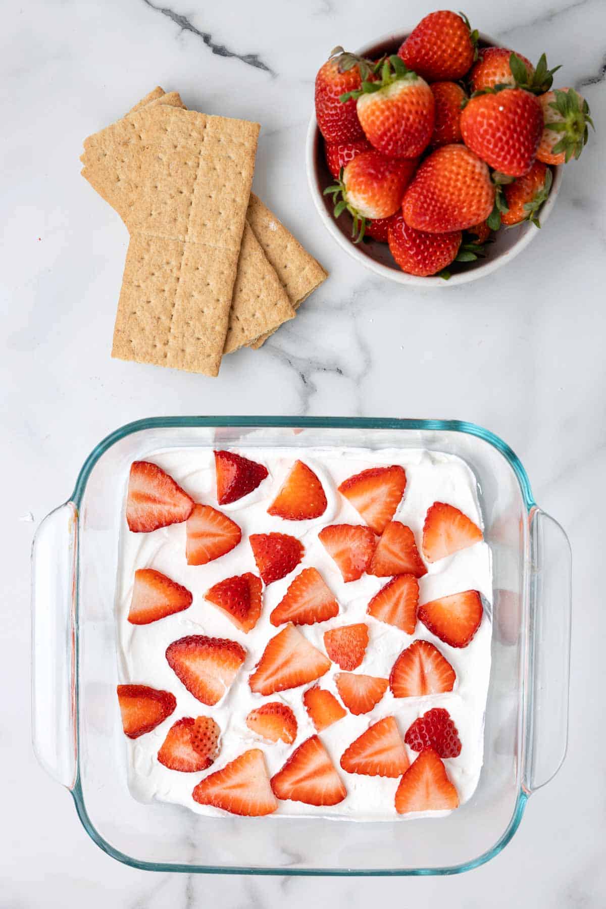 sliced strawberries on top of cool whip layer in a baking dish