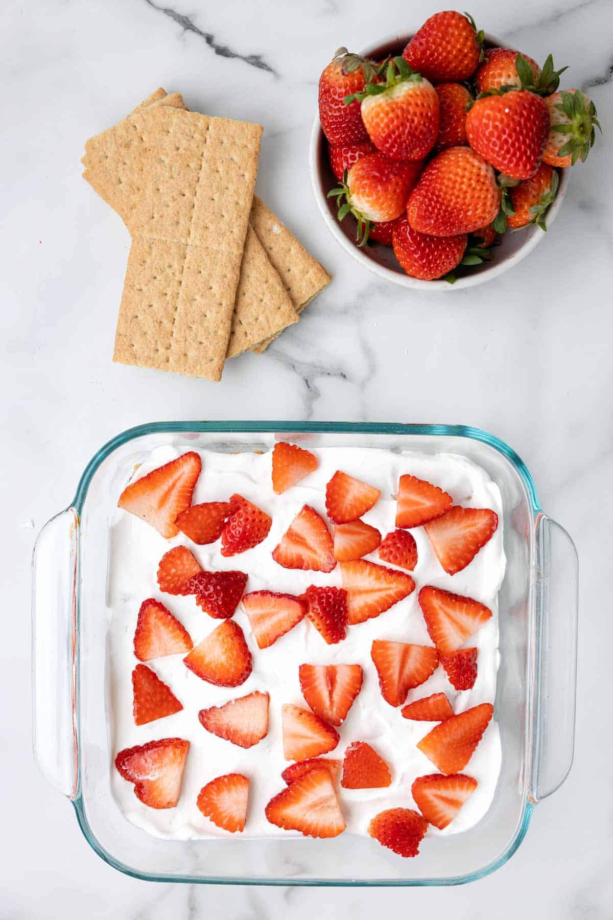 sliced strawberries on top of Cool whip in a baking dish
