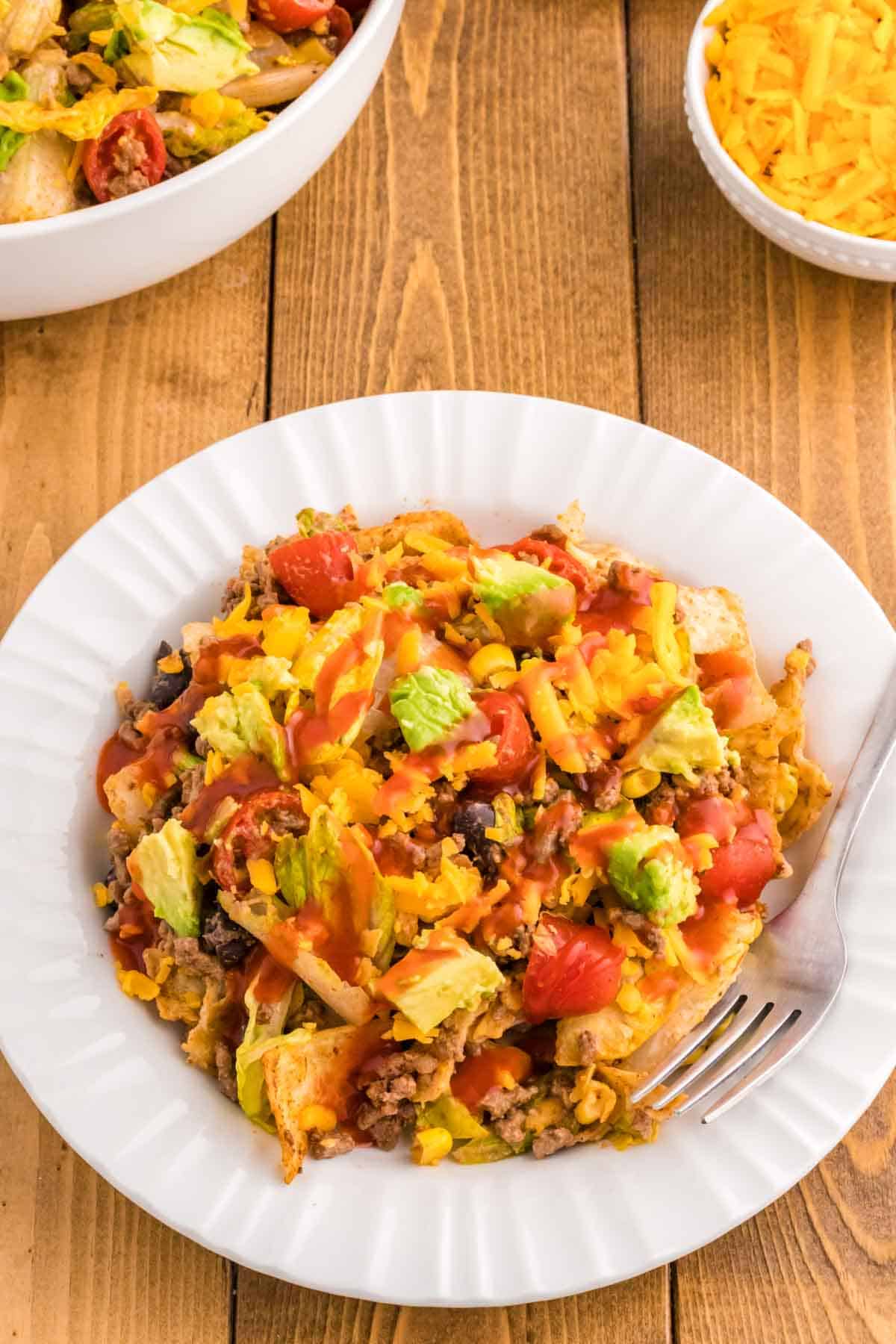 Taco Salad with Catalina Dressing is a hearty salad recipe loaded with taco seasoned ground beef, romaine lettuce, cherry tomatoes, cheddar cheese, crushed tortilla chips, corn, black bean and diced avocados all tossed in a sour cream and Catalina based dressing.