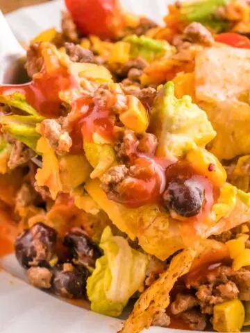 Taco Salad with Catalina Dressing is a hearty salad recipe loaded with taco seasoned ground beef, romaine lettuce, cherry tomatoes, cheddar cheese, crushed tortilla chips, corn, black bean and diced avocados all tossed in a sour cream and Catalina based dressing.