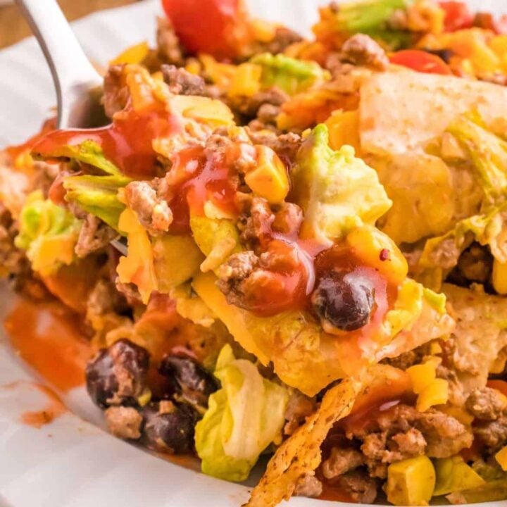 Taco Salad with Catalina Dressing is a hearty salad recipe loaded with taco seasoned ground beef, romaine lettuce, cherry tomatoes, cheddar cheese, crushed tortilla chips, corn, black bean and diced avocados all tossed in a sour cream and Catalina based dressing.