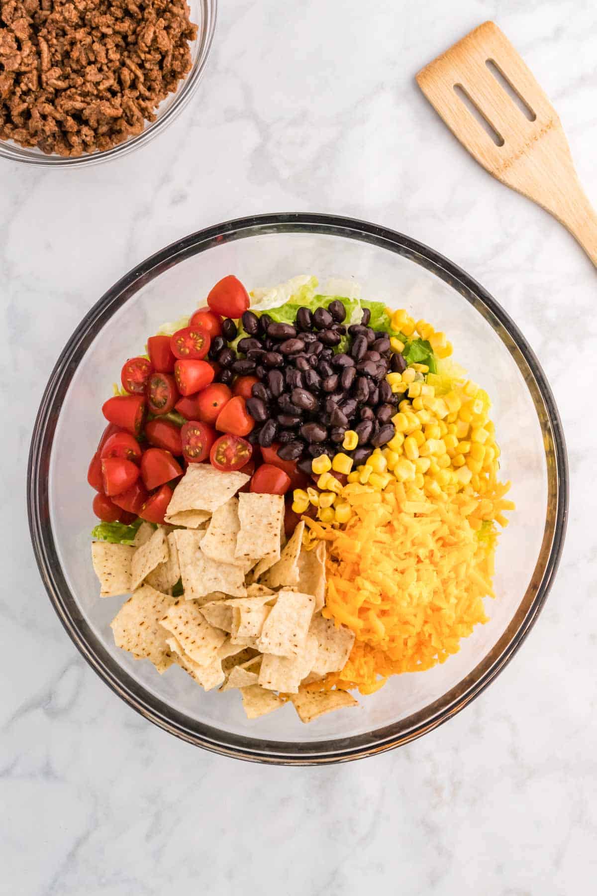 crumbled tortilla chips, shredded cheddar, corn, black beans and cherry tomatoes on top of chopped romaine in a bowl
