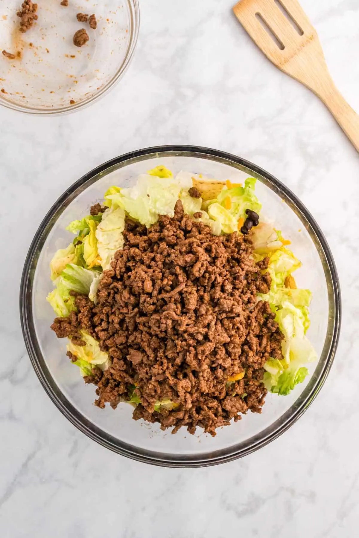 cooked ground beef on top of taco salad ingredients in a bowl