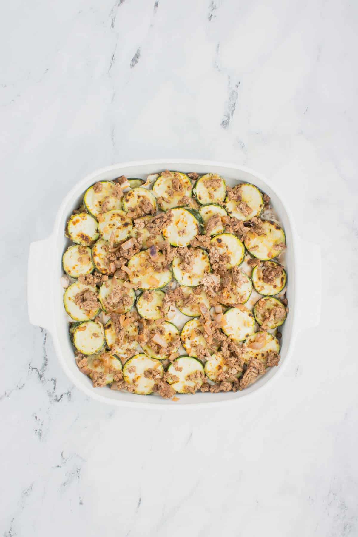 ground beef on top of zucchini slices in a baking dish