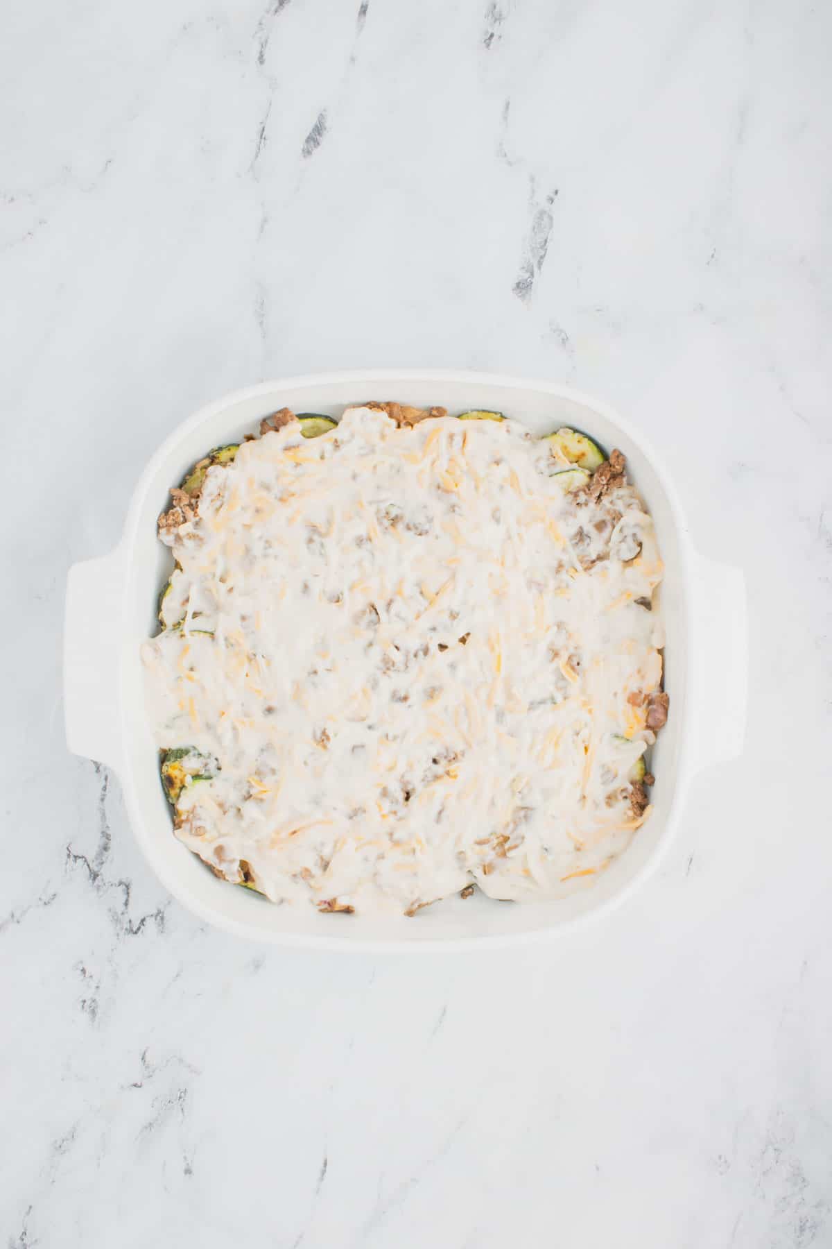 creamy soup and cheese mixture on top of ground beef and zucchini in a baking dish
