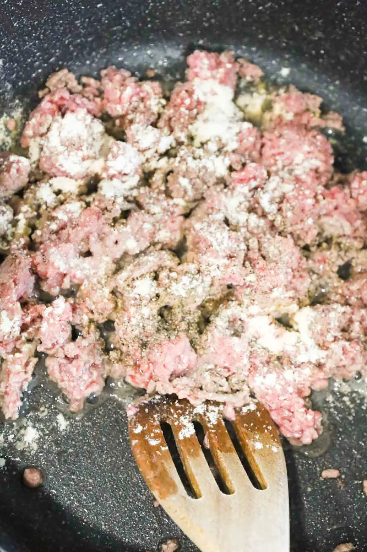 salt, pepper, garlic powder and onion powder added to ground beef cooking in a skillet