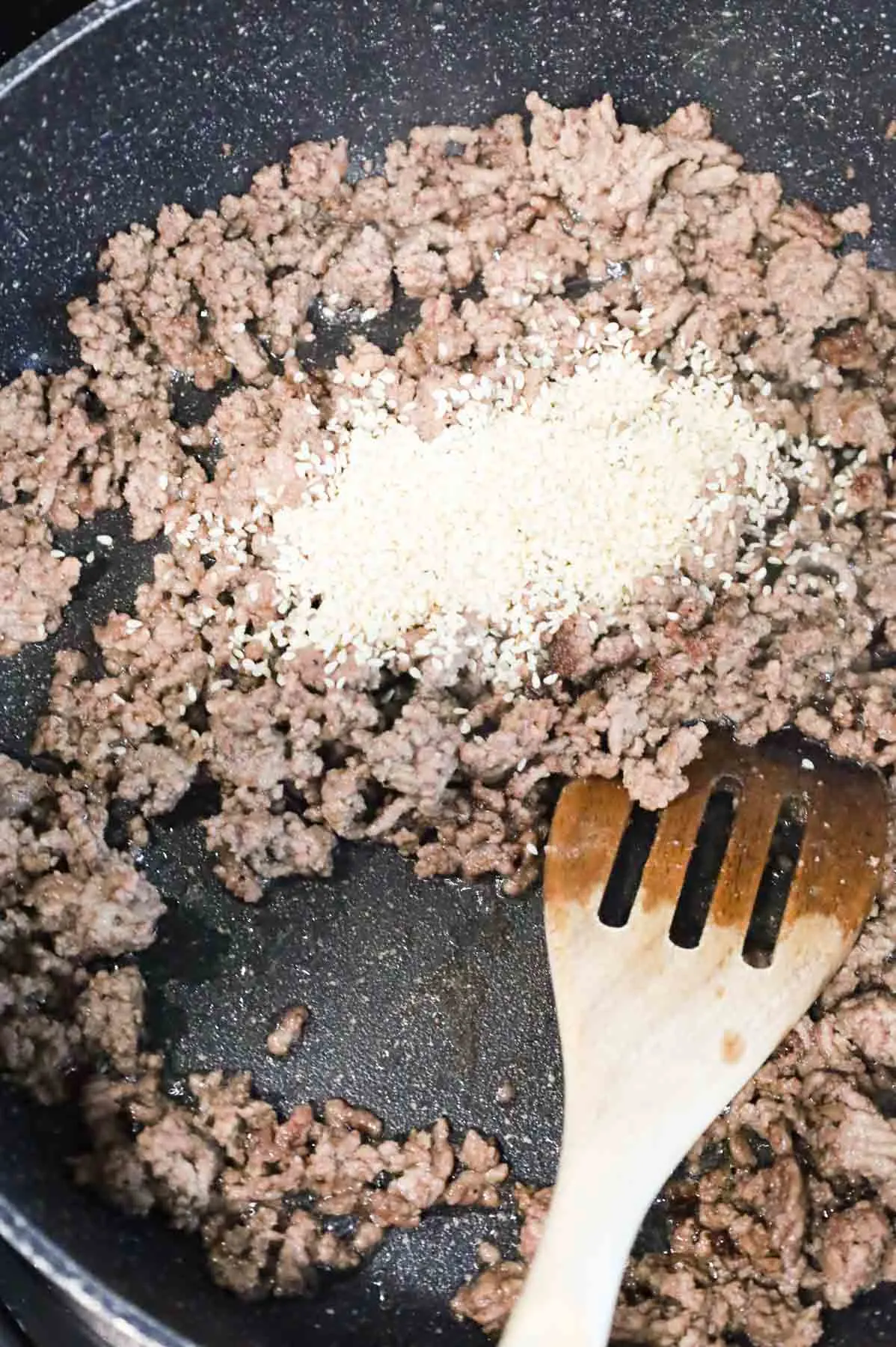 sesame seeds added to a skillet with cooked ground beef