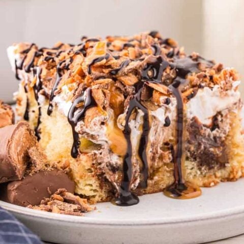 Butterfinger Poke Cake is a decadent dessert starting with a golden cake filled with chocolate and caramel sauce and topped with whipped topping and chopped Butterfinger chocolate bars.